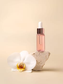 Dropper Bottle on stone near white orchid flowers on light yellow, close up, mockup. Skincare beauty product, essential oil or serum. Exotic cosmetics, pastel minimal composition..