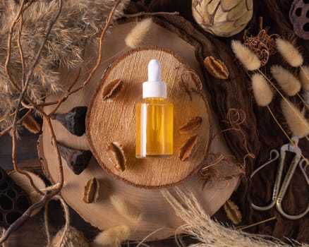 Dropper bottle with yellow liquid on wood near natural boho decorations top view, cosmetic packaging mockup. Skincare beauty product, serum or essence. Bohemian eco friendly flat lay with dried leaves.