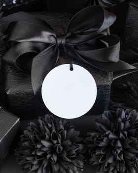 Wrapped Gift Boxes with black paper flowers and decorations and round gift tag, mockup, copy space. Dark composition with blank label card for Birthday, Anniversary or black party present