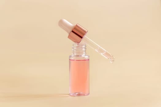 Opened Bottle with serum drop falling from pipette cap on light beige, close up, copy space. Skincare cosmetic product, essence or serum. Everyday beauty routine.