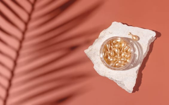 Face serum capsules in a jar on stone on pink top view, palm leaf hard shadows.. Skin care beauty product. Facial cosmetics, tropical minimal composition..