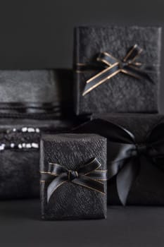 Black Gift Boxes with a ribbon bow on black close up. Wrapped presents for Dark themed Party, Christmas, Birthday, Anniversary. Black Friday concept. Monochrome composition