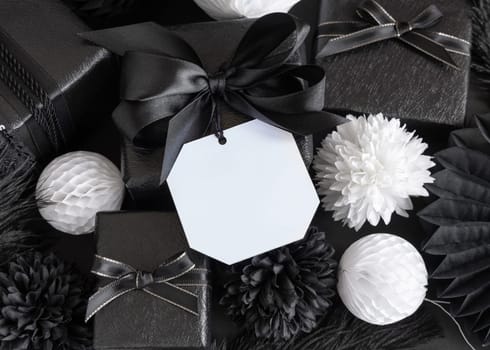 Gift Boxes with Black and white paper flowers and decorations, square gift tag Mockup, copy space. Dark composition with blank label card for Christmas, New Year, Birthday, Anniversary