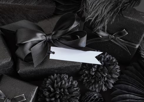 Wrapped Gift Boxes with black paper flowers and decorations and horizontal flag gift tag, mockup, copy space. Dark composition with blank label card for Birthday, Anniversary or black party present