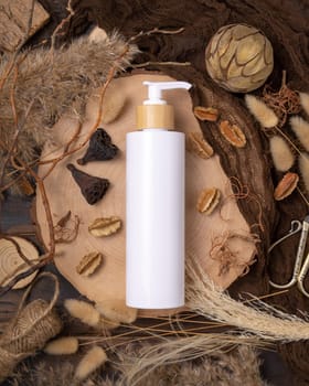 Refillable white one pump bottle on wood near natural boho decorations top view, label mockup. Skincare beauty product, lotion or essence. Bohemian eco friendly cosmetics flat lay with dried leaves.