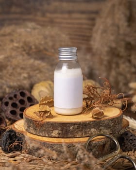 Cosmetic bottle with blank label on wood near natural decorations close up, package mockup. Eco friendly skincare product, lotion or cream. Bohemian composition with dried leaves and flowers.