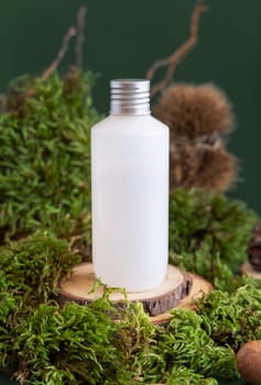 White plastic cream bottle on wooden piece between green moss and chestnuts, close up, mockup. Skincare beauty product package. Natural Organic Cosmetic concept. Biophilic composition