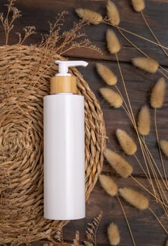 Cosmetic one pump bottle on boho wattled placemat near Hare's Tail grass top view on wood, label mockup. Natural skincare product, cream or lotion. Bohemian eco friendly beauty flat lay.