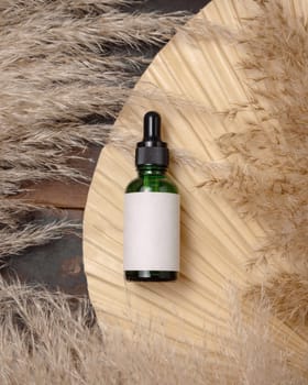 Cosmetic dropper bottle on dried palm leaf near pampas grass top view, label mockup. Skincare beauty product, lotion or essence. Bohemian eco friendly cosmetics flat lay with dried leaves.