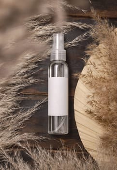 Transparent spray bottle on wood near dried palm leaf and pampas grass top view, label mockup. Skincare beauty product, cleanser or water. Bohemian eco friendly cosmetics flat lay with dried leaves.