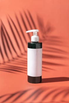 One pump Plastic bottle with blank label on red, palm leaf hard shadows, close up, mockup. Skincare beauty product, facial cleaner or lotion. Beauty routine with natural cosmetics..