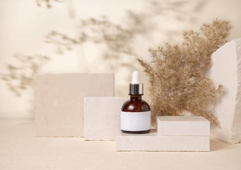 Brown dropper bottle with blank label on stones near pampas grass on light beige close up, packaging mockup. Skincare beauty product, lotion or cleanser. Natural eco friendly cosmetics