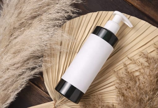 Cosmetic one pump bottle on dried palm leaf near pampas grass top view, label mockup. Skincare beauty product, lotion or essence. Bohemian eco friendly cosmetics flat lay with dried leaves.