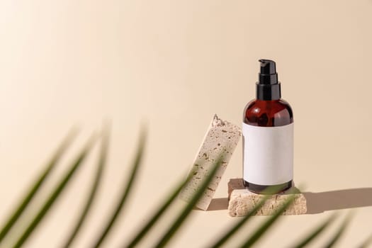 Glass cosmetic one pump bottle on stone on light beige with a palm leaf, close up, label mockup. Skincare beauty product, lotion or essence. Natural cosmetics.