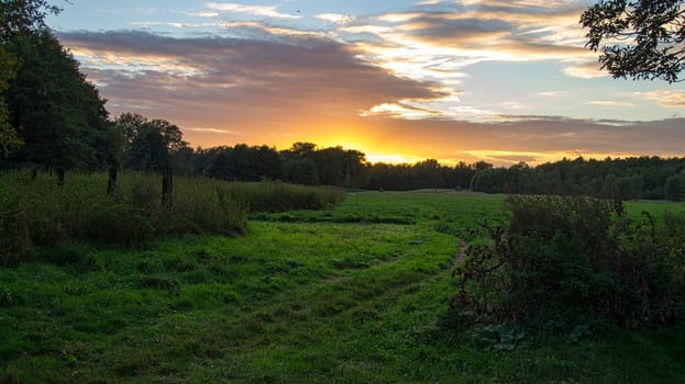 Field path across a meadow to the sunset. The sky shines fabenfoh in all colors