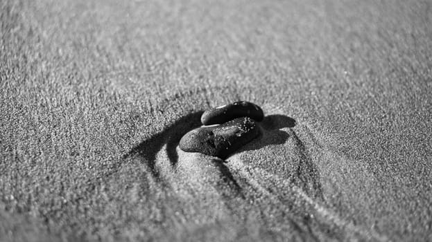 heart-shaped stone in the sand of the beach on the Baltic Sea black and white. Romantic symbol for people in love. Small sign as still life.