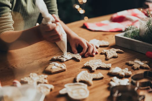 Christmas food preparation. Gingerbread cooking, decorating freshly baked cookies with icing and mastic. Little girl decorate cookie. Closeup on cropped shot with toddler kid hands holding icing pack