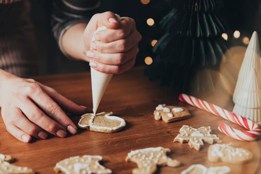 Christmas, New Year food preparation. Xmas gingerbread cooking, making and decorating freshly baked cookies. Closeup on cropped shot with woman hands holding icing and mastic, decorating cookies