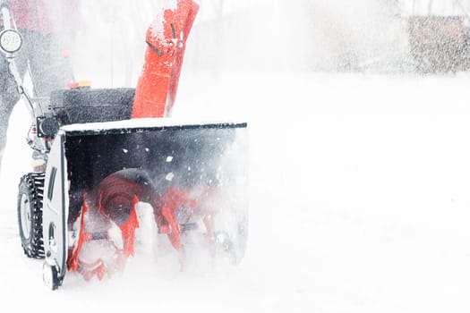 Detail closeup of portable red snow blower powered by gasoline in action. Man outdoor using snowblower machine after snowstorm, snowfall for clearing, removing snow. Snow removal, thrower assistant