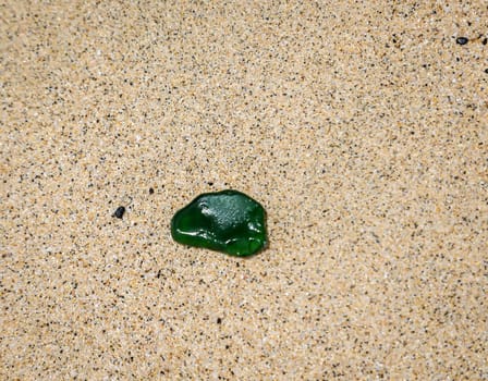 A green glass pane on the beach. A so-called sea glass.