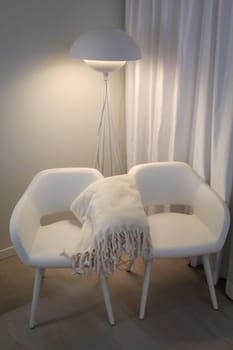 Detail of a room interior with two white armchairs and wool blanket.