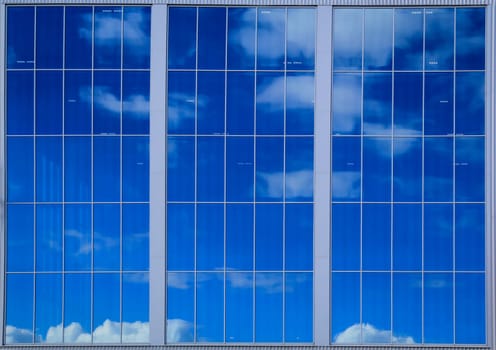 A large industrial building window in which the sky and clouds are reflected.