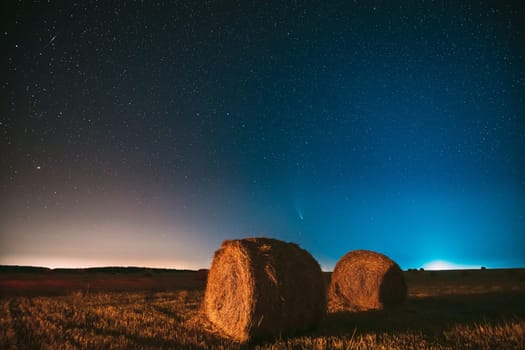Comet Neowise C2020 F3 In Night Starry Sky Above Haystacks In Summer Agricultural Field. Night Stars Above Rural Landscape With Hay Bales After Harvest.