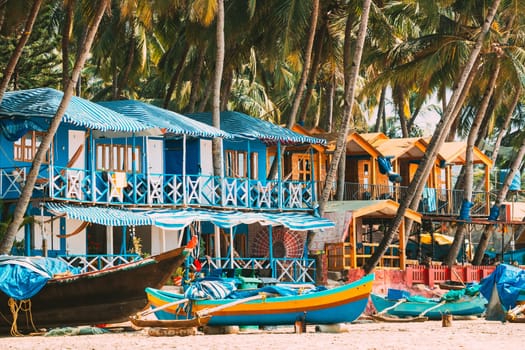 Canacona, Goa, India. Fishing Boat And Famous Painted Guest Houses On Palolem Beach Against Background Of Tall Palm Trees In Sunny Day.