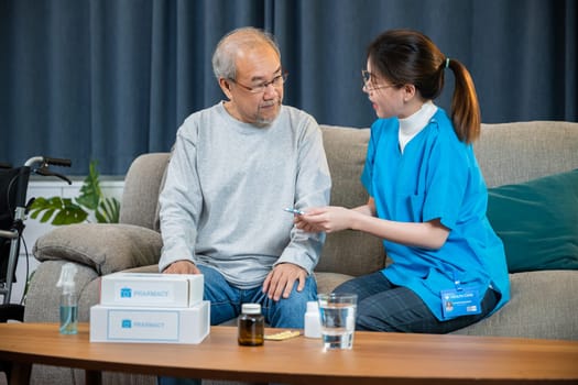 Woman nurse caregiver showing prescription drug to senior man at nursing home, healthcare support, Asian doctor with physician visit senior male patient consult medicine dosage at house in living room