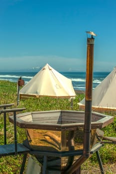 The Glamping house and outdoor bath tub on ocean coast, rural landscape, tent houses in Kamchatka peninsula. Selective focus.
