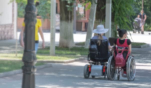 The blurred view of two disabled person on an electric wheelchair on a city street .