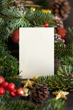 Vertical blank card between decorations, fir branches and pine cones close up, mockup. Christmas or New Year greeting card template, Holiday or wedding stationery
