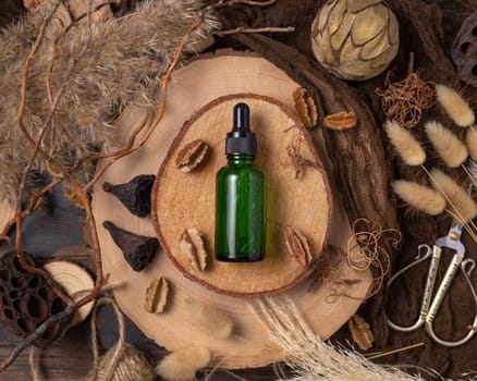 Green cosmetic dropper bottle with liquid on wood near natural boho decorations top view. Skincare beauty product, serum or essence. Bohemian eco friendly flat lay with dried leaves.
