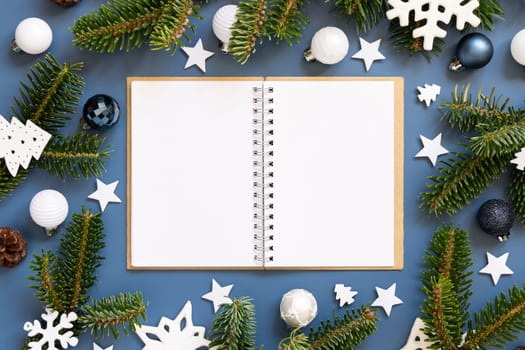 Blank open notepad on a blue background near white Christmas decorations and fir branches top view. New Year Textbook mockup flat lay, copy space. Planning and organizing concept