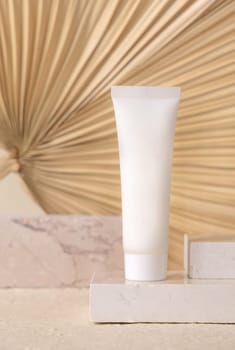 White blank tube on travertine stone against dry beige palm leaf close up, mockup. Skincare beauty product - cream or lotion. Natural organic cosmetics. Minimal eco friendly composition..
