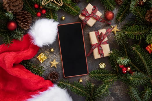 Mobile phone between Christmas decorations, wrapped gift boxes and green fir branches top view. Cell phone mockup with copy space. Christmas or New Year Holiday atmospheric flat lay