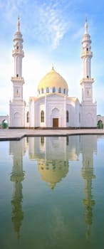 White Mosque, Bolgar, Tatarstan. A beautiful white mosque with domes and minarets against a bright blue sky. In the foreground is a reflection in the water.
