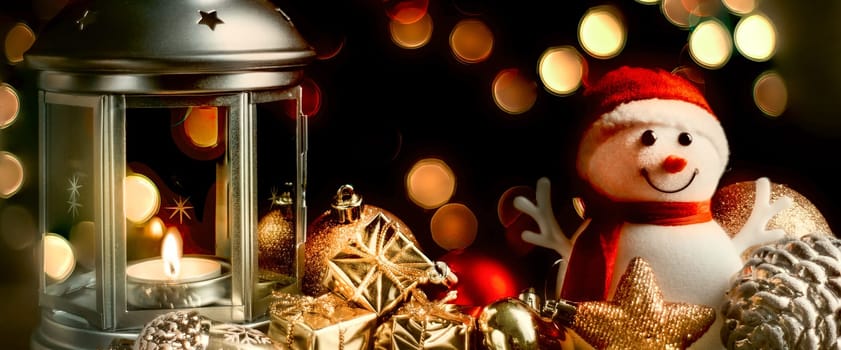 Christmas composition: A snowman, a lantern with candles, bright shiny boxes with gifts, blurred bokeh lights in the background.