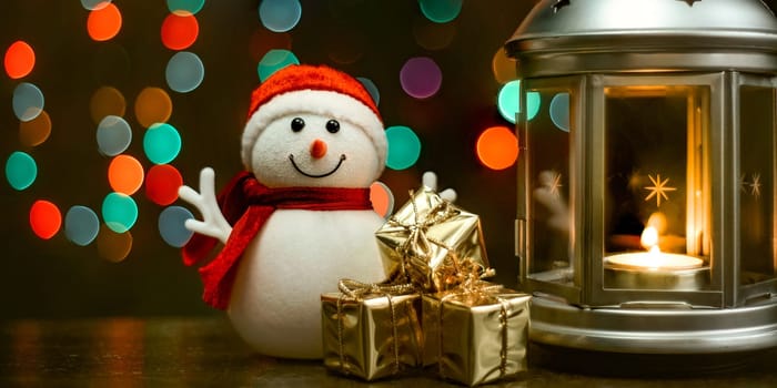 Christmas composition: A snowman, a lantern with candles, bright shiny boxes with gifts, blurred bokeh lights in the background.