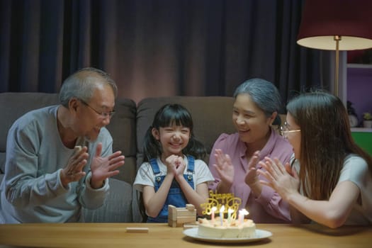 Birthday surprise. Happy Asian family grandparents and mother celebrating enjoy birthday party with cake of granddaughter at home in night time