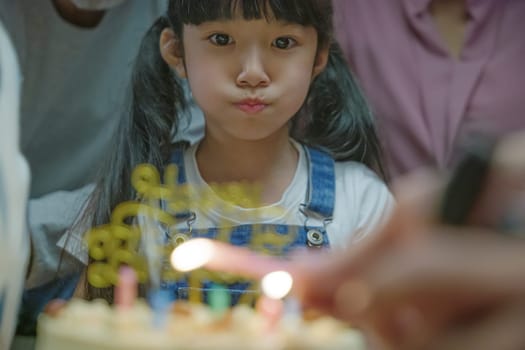 Happy Asian family grandparents and mother celebrating enjoy singing birthday song party with cake of granddaughter blowing candle at home in night time, Birthday surprise concept