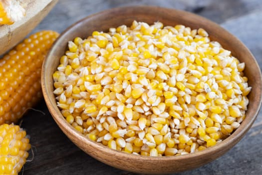 Popcorn kernels in a wooden bowl with popcorn on the cob
