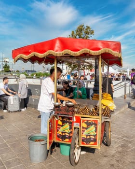 Istanbul, Turkey - August 30, 2022: Young man selling chestnut and corn on traditional Turkish fast food cart at Eminonu Piazza