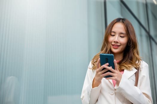 Asian businesswoman texting smartphone commuting work she walking near her office building in morning, Beautiful business woman smiling hold mobile phone outdoor walking on city street urban