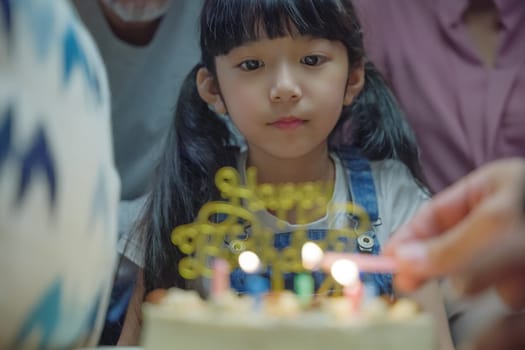 Birthday surprise. Happy Asian family grandparents and mother celebrating enjoy birthday party with cake of granddaughter at home in night time