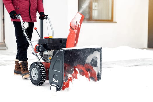 Closeup of red snow blower in action. Senior mature man outdoor in front of house using snowblower machine for removing snow on yard. Snow thrower in winter outside home. Young worker guy blowing snow
