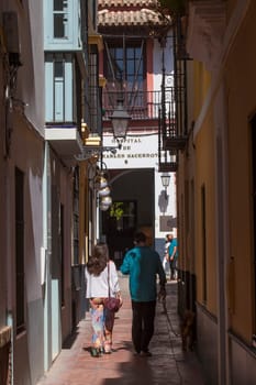 Seville, Spain - Sept 27th, 2020: Tourist couple walking the dog by narrow street of Santa Cruz neighborhood, historic district of Seville, Spain