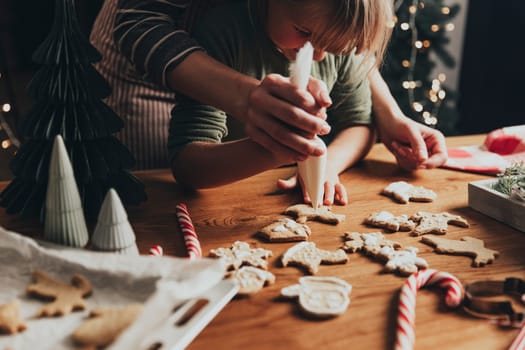 Christmas and New Year food preparation. Xmas gingerbread cooking and decorating freshly baked cookies with icing and mastic. Mom helping cute little daughter to decorate cookie on wooden messy table