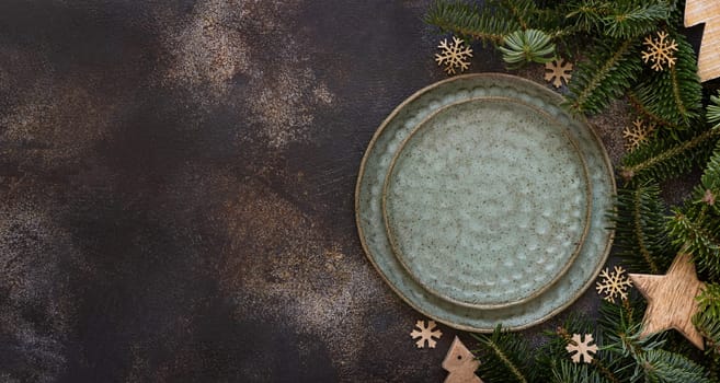 Festive table setting with fir tree branches and Rustic wooden decorations top view, copy space,. Christmas or New Year table place with green plates on dark table flat lay. Winter season, restaurant catering