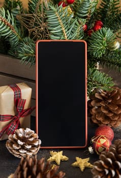 Mobile phone between Christmas decorations, wrapped gift boxes and green fir branches close up. Cell phone mockup with copy space. Christmas or New Year Holiday atmospheric composition
